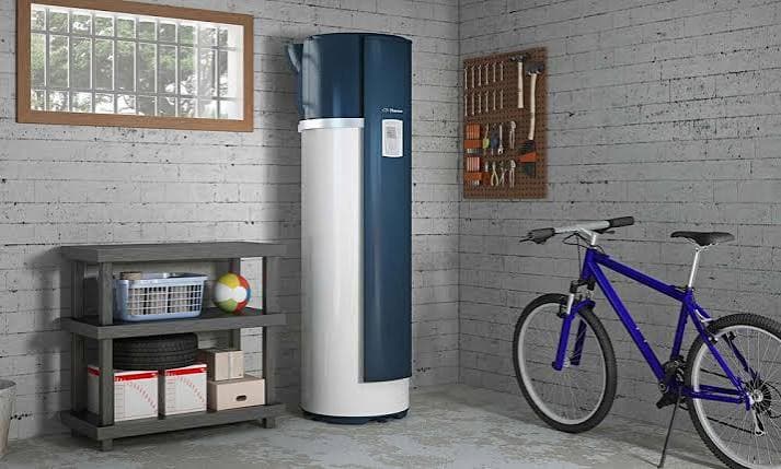 Chauffe-eau thermodynamique blanc et bleu dans un garage avec un vélo et des outils.